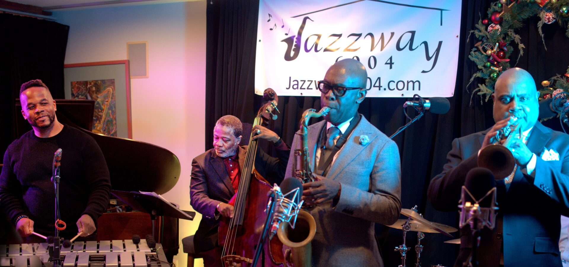 A man in grey suit and glasses playing the saxophone.