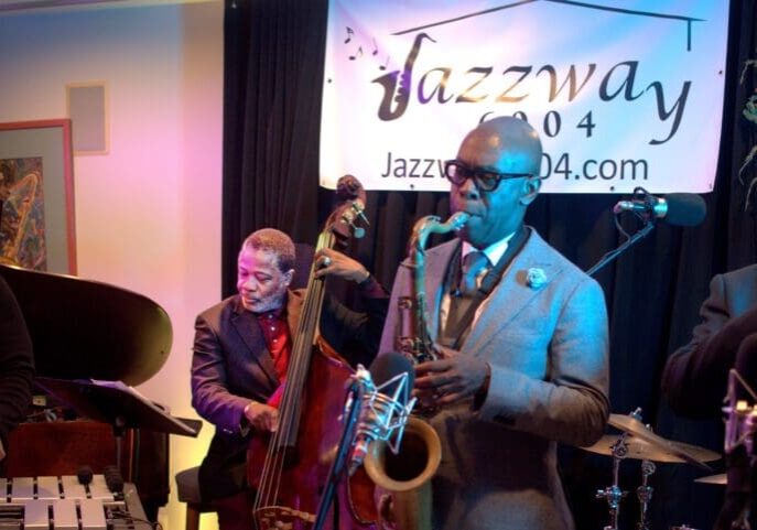 A man in grey suit and glasses playing the saxophone.